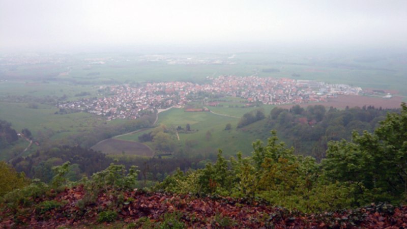 Blick von einem Hügel auf eine Stadt in der Ferne, umgeben von grünen Feldern und Bäumen. Der Himmel ist bewölkt und neblig., © Schwäbische Alb Tourismusverband e.V. Blick von einem Hügel auf eine Stadt in der Ferne, umgeben von grünen Feldern und Bäumen. Der Himmel ist bewölkt und neblig., © Schwäbische Alb Tourismusverband e.V.