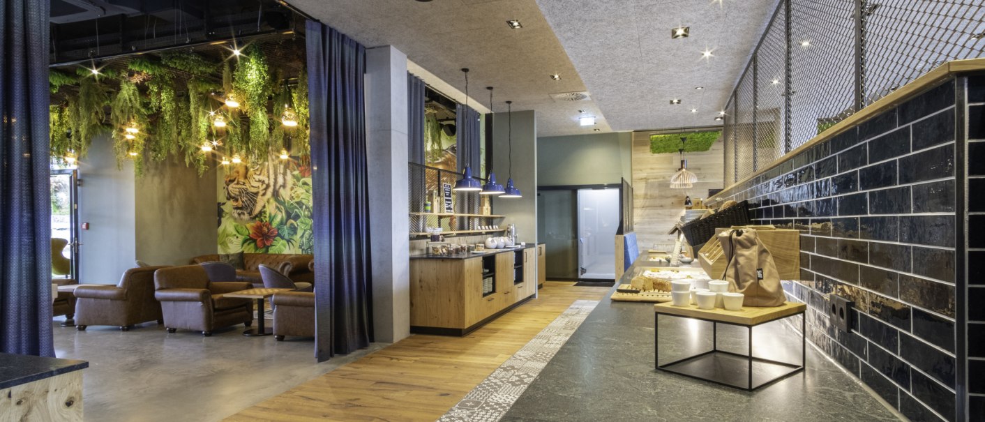 Moderner Frühstücksbereich mit hängenden Pflanzen, gemütlichen Sitzgelegenheiten und einem Buffet mit Geschirr und Speisen., © 13 6 Design GmbH (Judenhof 10, 89073 Ulm)