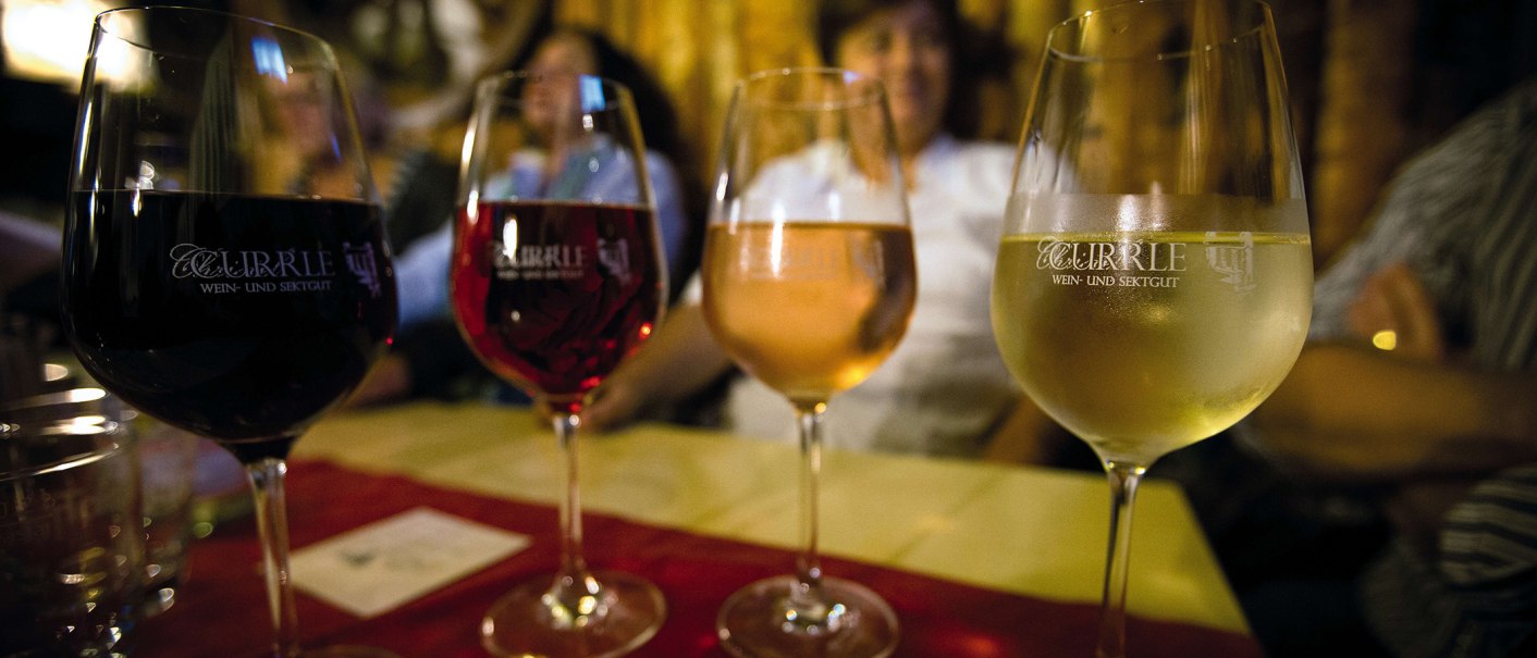 Vier Weingläser mit unterschiedlichen Weinsorten stehen auf einem Tisch. Im Hintergrund sind unscharf Personen zu erkennen., © Stuttgart-Marketing GmbH