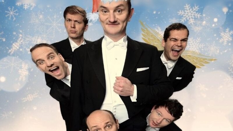 Fünf Männer in Frack posieren humorvoll vor einem winterlichen Hintergrund mit Schneeflocken. Einer trägt eine Weihnachtsmütze, ein anderer Engelsflügel., © Touristik Bad Wildbad GmbH