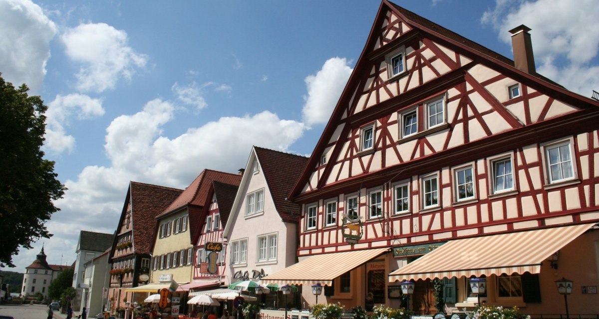 Fachwerkhäuser in Langenburg, Deutschland, mit bunten Fassaden und Geschäften. Im Hintergrund ist ein Schloss zu sehen. Der Himmel ist blau mit Wolken., © Touristikgemeinschaft Hohenlohe, Künzelsau / Marion Schlund Fachwerkhäuser in Langenburg, Deutschland, mit bunten Fassaden und Geschäften. Im Hintergrund ist ein Schloss zu sehen. Der Himmel ist blau mit Wolken., © Touristikgemeinschaft Hohenlohe, Künzelsau / Marion Schlund