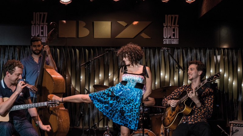 Eine Band spielt im BIX Jazzclub. Ein Gitarrist, ein Kontrabassist und eine Sängerin in blauem Kleid sind zu sehen. "Jazz Open Stuttgart" im Hintergrund., © Peter Steinheisser Eine Band spielt im BIX Jazzclub. Ein Gitarrist, ein Kontrabassist und eine Sängerin in blauem Kleid sind zu sehen. "Jazz Open Stuttgart" im Hintergrund., © Peter Steinheisser