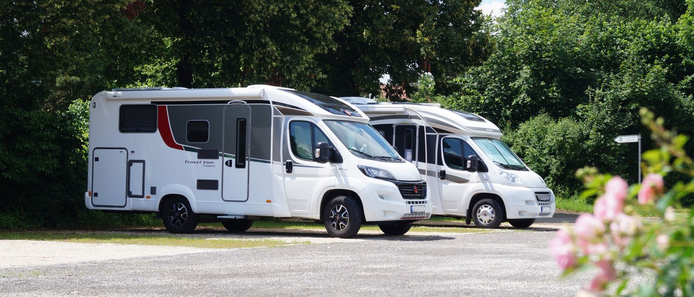 Zwei Wohnmobile stehen auf einem Stellplatz, umgeben von grünen Bäumen. Im Vordergrund sind unscharfe rosa Blumen zu sehen., © Stadt Nürtingen, Clint Metzger