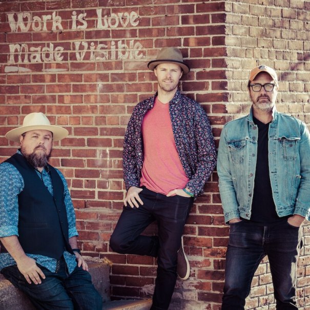 Drei M&auml;nner posieren l&auml;ssig vor einer Backsteinmauer mit dem Schriftzug 'Work is love made visible'., &copy; Mauerwerk GmbH