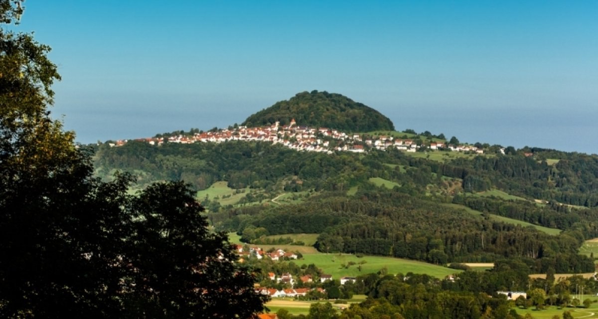 Der Hohenstaufen erhebt sich majestätisch über die umliegende Landschaft, umgeben von grünen Wäldern und kleinen Dörfern unter einem klaren blauen Himmel., © Landratsamt Göppingen Der Hohenstaufen erhebt sich majestätisch über die umliegende Landschaft, umgeben von grünen Wäldern und kleinen Dörfern unter einem klaren blauen Himmel., © Landratsamt Göppingen