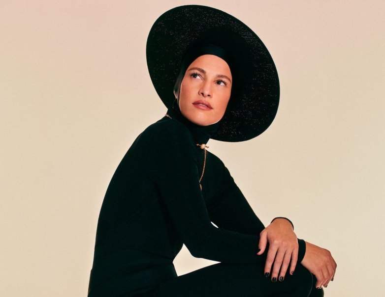 Eine Person in einem eleganten schwarzen Outfit mit gro&szlig;em Hut sitzt und blickt nachdenklich zur Seite., &copy; Carminho &copy; Fernando Tomaz