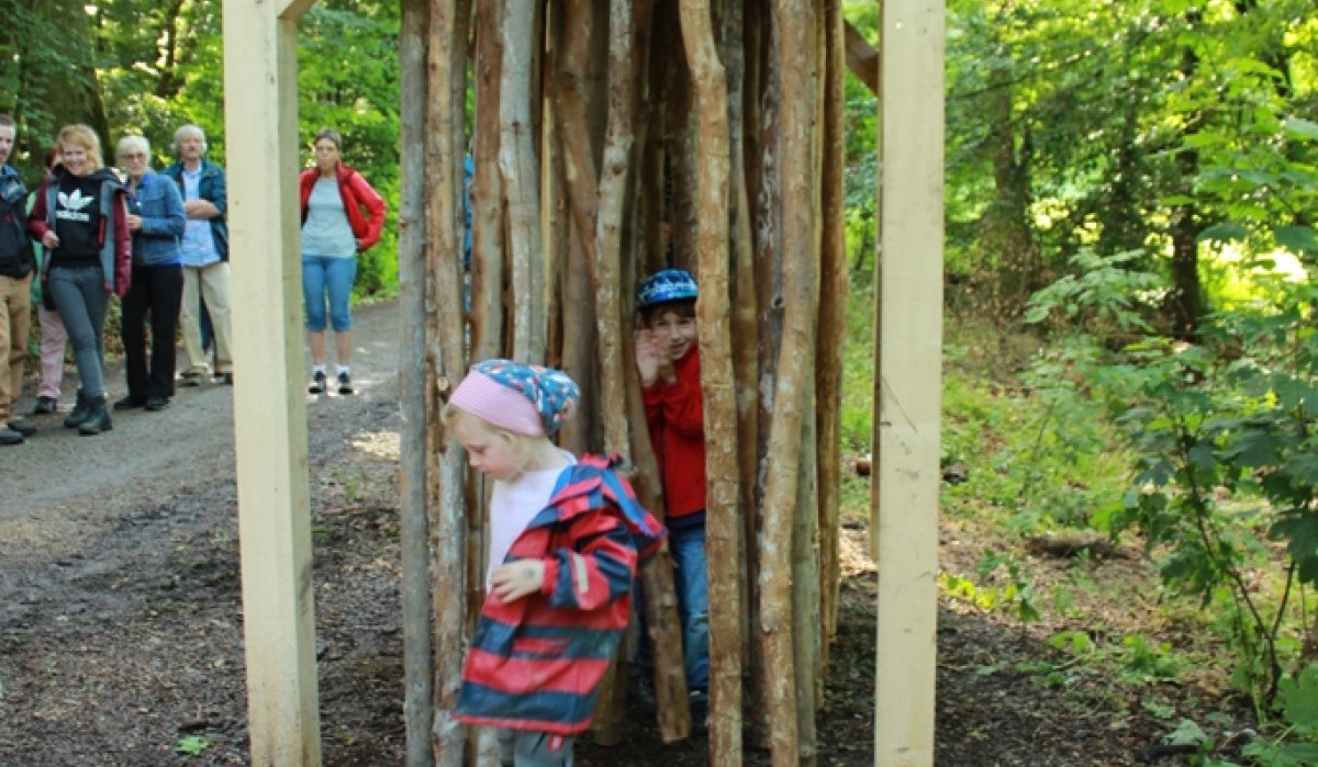Kinder spielen in einer Holzkonstruktion aus Holzstämmen im Wald. Im Hintergrund stehen Erwachsene und beobachten die Szene., © Amt für Forsten Landkreis Böblingen Kinder spielen in einer Holzkonstruktion aus Holzstämmen im Wald. Im Hintergrund stehen Erwachsene und beobachten die Szene., © Amt für Forsten Landkreis Böblingen