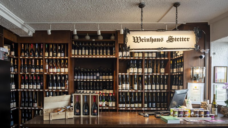 Theke im Weinhaus Stetter mit Regalen voller Weinflaschen und einem hölzernen Tresen. Ein Schild mit der Aufschrift 'Weinhaus Stetter' hängt von der Decke., © Stuttgart Marketing GmbH, Sarah Schmid Theke im Weinhaus Stetter mit Regalen voller Weinflaschen und einem hölzernen Tresen. Ein Schild mit der Aufschrift 'Weinhaus Stetter' hängt von der Decke., © Stuttgart Marketing GmbH, Sarah Schmid