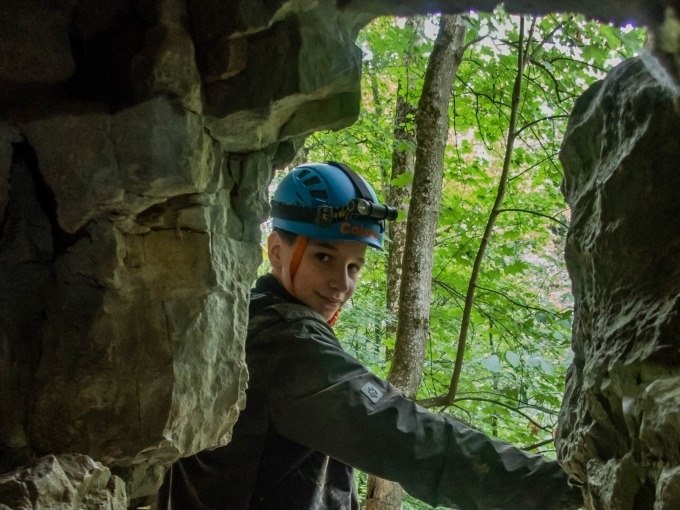Eine Person mit Helm steht in einer H&ouml;hlen&ouml;ffnung und schaut nach drau&szlig;en in einen gr&uuml;nen Wald., &copy; SwabianTravel