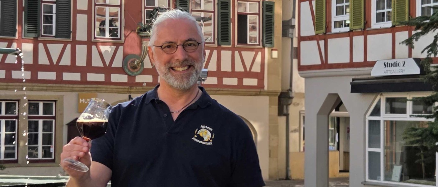 Ein Mann mit Brille und Bart h&auml;lt ein Bierglas vor Fachwerkh&auml;usern in Leonberg. Ein Schild mit 'Studio 2 Artgallery' ist im Hintergrund sichtbar., &copy; Stadtmarketing Leonberg