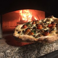 Eine frisch gebackene Pizza mit Tomaten und Kräutern wird aus einem heißen Holzofen geholt. Der Ofen ist aus Stein und das Feuer lodert., © cDaCarmine Eine frisch gebackene Pizza mit Tomaten und Kräutern wird aus einem heißen Holzofen geholt. Der Ofen ist aus Stein und das Feuer lodert., © cDaCarmine