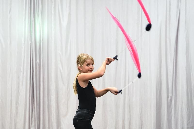 Ein Mädchen jongliert mit pinken Bändern vor einem grauen Vorhang. Sie trägt ein schwarzes Outfit und wirkt konzentriert., © Kunstschule Labyrinth