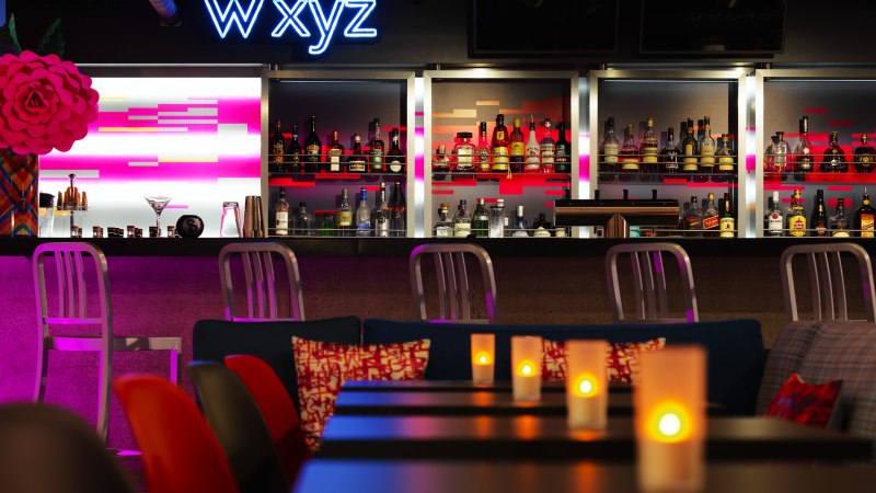 Moderne Bar mit Neon-Schriftzug 'W XYZ', beleuchtetem Tresen und gemütlicher Atmosphäre. Kerzen auf den Tischen sorgen für stimmungsvolles Licht., © Aloft Stuttgart