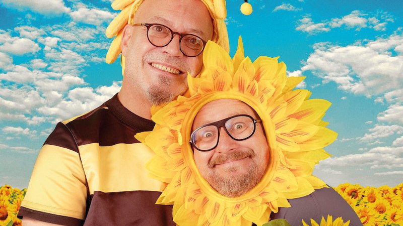 Zwei Personen in Bienen- und Sonnenblumenkostümen lächeln vor einem Sonnenblumenfeld und blauem Himmel. Fröhliche und bunte Szene., © Scala Kultur Live gGmbH Zwei Personen in Bienen- und Sonnenblumenkostümen lächeln vor einem Sonnenblumenfeld und blauem Himmel. Fröhliche und bunte Szene., © Scala Kultur Live gGmbH