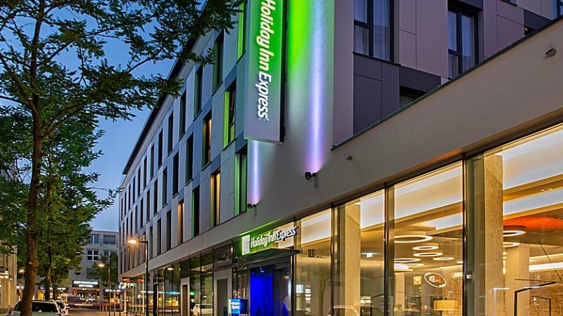 Au&szlig;enansicht eines modernen Holiday Inn Express Hotels bei D&auml;mmerung, mit beleuchtetem Logo und Glasfassade., &copy; Holiday Inn Express Waiblingen