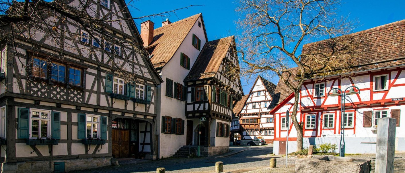 Fachwerkhäuser in der Altstadt von Sindelfingen, die unter blauem Himmel erstrahlen. Ein Baum ohne Blätter steht im Vordergrund., © Stuttgart-Marketing GmbH, Sarah Schmid Fachwerkhäuser in der Altstadt von Sindelfingen, die unter blauem Himmel erstrahlen. Ein Baum ohne Blätter steht im Vordergrund., © Stuttgart-Marketing GmbH, Sarah Schmid