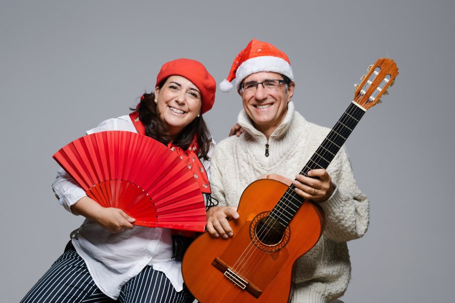 Ein Mann und eine Frau tragen Weihnachtsm&uuml;tzen. Die Frau h&auml;lt einen roten F&auml;cher, der Mann eine Gitarre. Beide l&auml;cheln in die Kamera., &copy; Duo Alegria