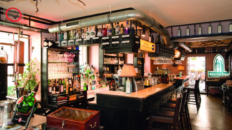 Bar mit Flaschen, Gläsern und Kupferdestille. Klosterfrau-Logo leuchtet im Hintergrund. Gemütliche Atmosphäre mit Holzmöbeln und Lampen., © Buschwerk Mediendesign-Wilhelmer Gastronomie