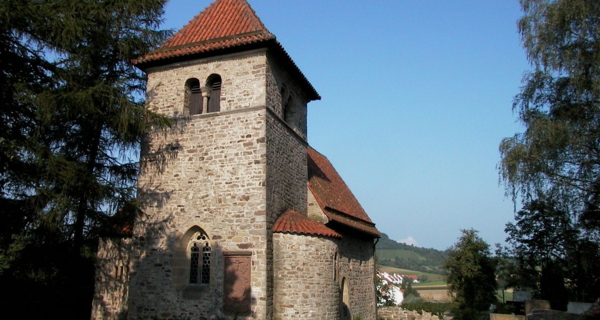 Romanische Kirche mit rotem Ziegeldach und Glockenturm, umgeben von Bäumen und Landschaft. Der Himmel ist klar und blau., © Tourismusgemeinschaft Marbach-Bottwartal