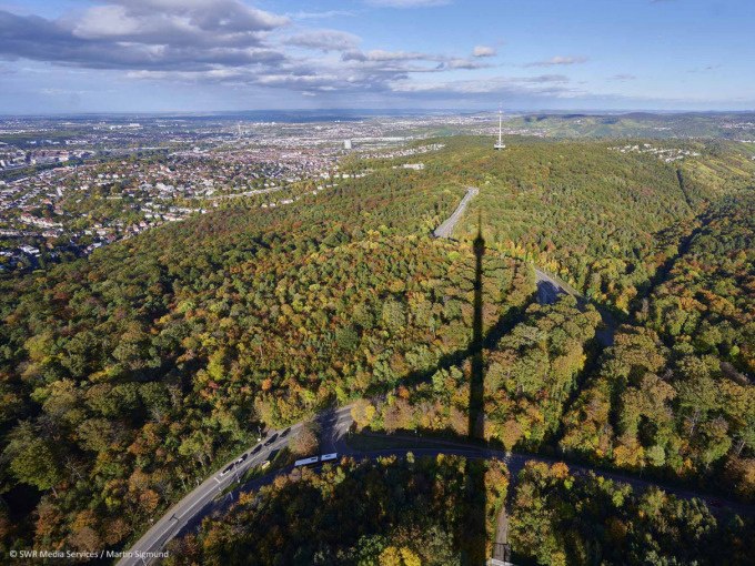 Luftaufnahme des Stuttgarter Fernsehturms, dessen Schatten &uuml;ber einen bewaldeten H&uuml;gel f&auml;llt. Im Hintergrund sind Stadt und H&uuml;gel zu sehen., &copy; SWR Media Services GmbH / Fernsehturm Stuttgart