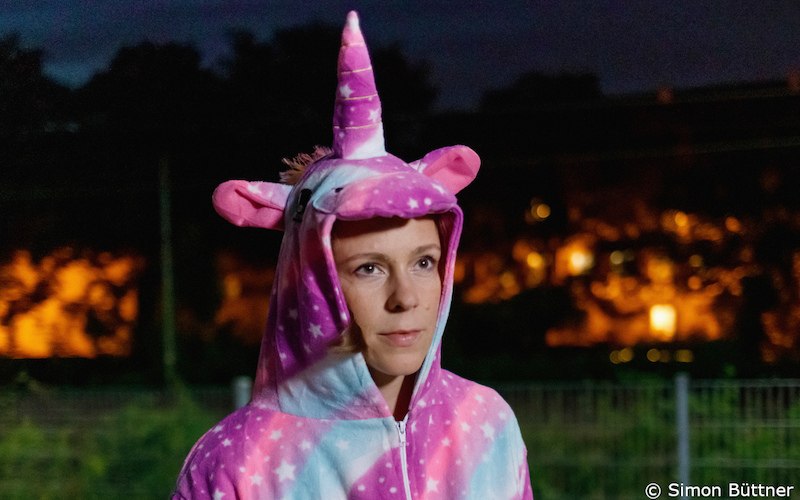 Eine Person trägt ein pinkes Einhorn-Kostüm mit Kapuze. Der Hintergrund ist unscharf und zeigt Lichter in der Nacht., © Kultur- und Sportamt Stadt Bietigheim-Bissingen