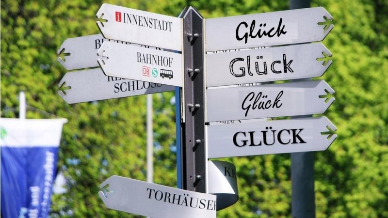 Ein Wegweiser zeigt in verschiedene Richtungen, darunter zur Innenstadt, zum Bahnhof und mehrmals zum Gl&uuml;ck. Der Hintergrund ist gr&uuml;n und bewaldet., &copy; Pixabay