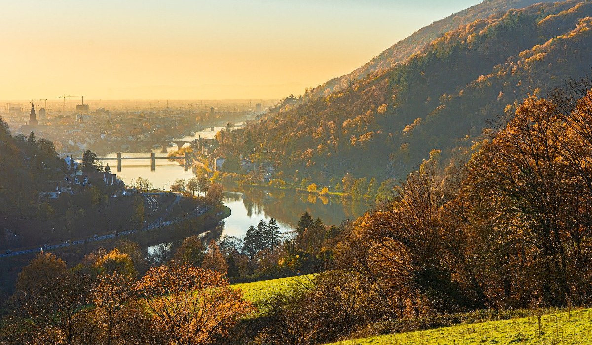 Herbstliche Landschaft am Neckar mit Brücke und Stadt im Hintergrund, umgeben von Hügeln und Bäumen im goldenen Licht der Abenddämmerung. Herbstliche Landschaft am Neckar mit Brücke und Stadt im Hintergrund, umgeben von Hügeln und Bäumen im goldenen Licht der Abenddämmerung.