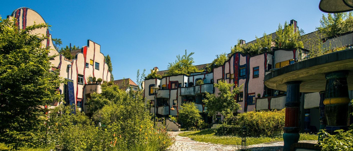 Das Hundertwasserhaus in Plochingen zeigt bunte, wellenf&ouml;rmige Fassaden und begr&uuml;nte D&auml;cher unter einem klaren blauen Himmel., &copy; Stuttgart-Marketing GmbH, Sarah Schmid