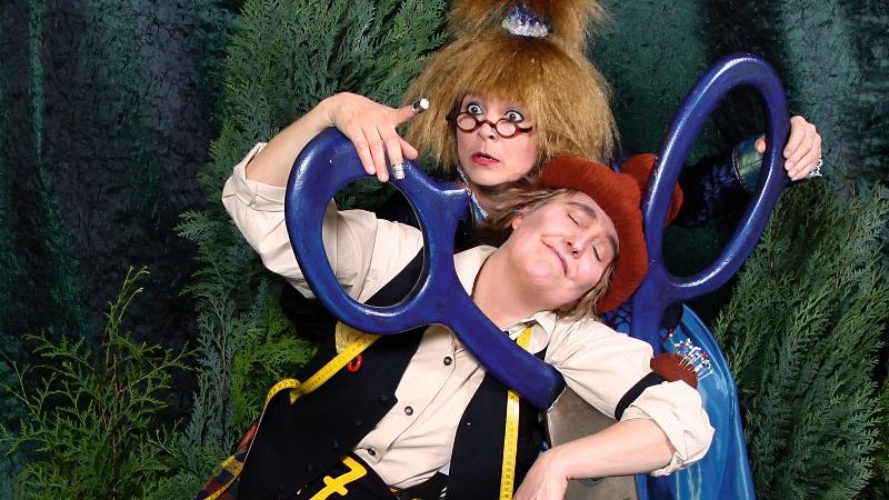 Zwei Personen in fantasievollen Kostümen posieren mit einer übergroßen Schere vor einem grünen Hintergrund., © Backnang Zwei Personen in fantasievollen Kostümen posieren mit einer übergroßen Schere vor einem grünen Hintergrund., © Backnang