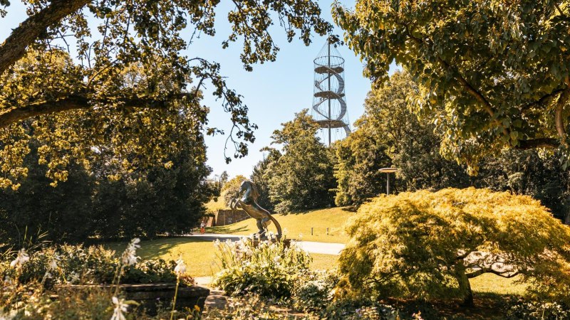 Ein grüner Park mit Bäumen, einer Pferdeskulptur und einem spiralförmigen Aussichtsturm im Hintergrund., © Stuttgart-Marketing GmbH, Sarah Schmid Ein grüner Park mit Bäumen, einer Pferdeskulptur und einem spiralförmigen Aussichtsturm im Hintergrund., © Stuttgart-Marketing GmbH, Sarah Schmid