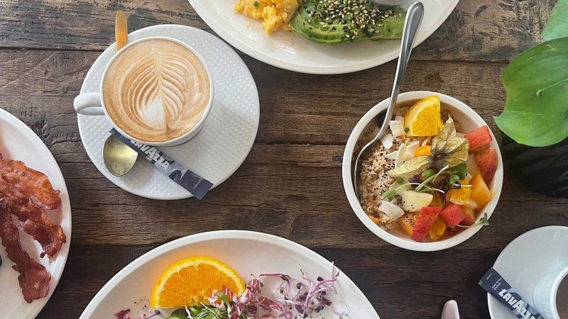 Ein reich gedeckter Frühstückstisch mit Kaffee, Pancakes mit Speck, Avocado mit Rührei und einer Schale mit frischem Obst., © SMG Ein reich gedeckter Frühstückstisch mit Kaffee, Pancakes mit Speck, Avocado mit Rührei und einer Schale mit frischem Obst., © SMG