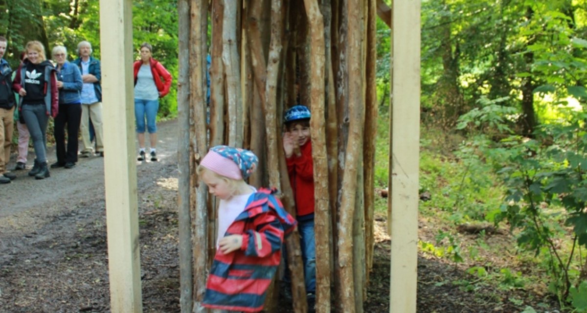 Kinder spielen in einer Holzkonstruktion aus Holzstämmen im Wald. Im Hintergrund stehen Erwachsene und beobachten die Szene., © Amt für Forsten Landkreis Böblingen Kinder spielen in einer Holzkonstruktion aus Holzstämmen im Wald. Im Hintergrund stehen Erwachsene und beobachten die Szene., © Amt für Forsten Landkreis Böblingen