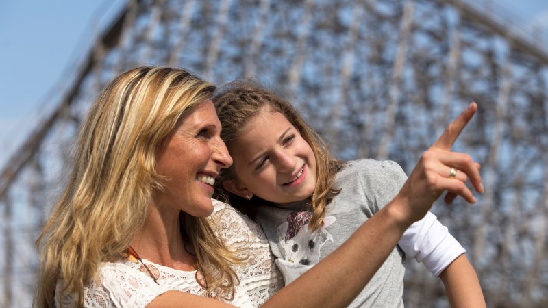 Eine Frau und ein Mädchen lächeln und zeigen in die Ferne. Im Hintergrund ist eine unscharfe Struktur zu sehen., © Erlebnispark Tripsdrill Eine Frau und ein Mädchen lächeln und zeigen in die Ferne. Im Hintergrund ist eine unscharfe Struktur zu sehen., © Erlebnispark Tripsdrill