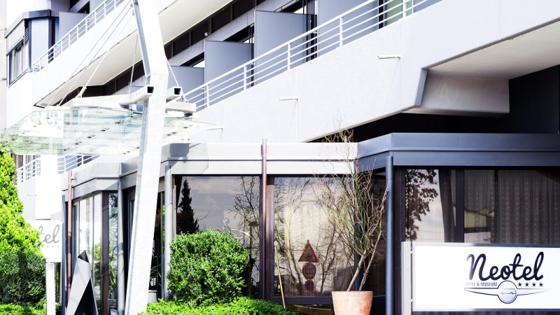 Eingang des Hotels Neotel mit Glasvordach und moderner Fassade. Ein Schild mit dem Hotelnamen ist sichtbar. Grüne Pflanzen umrahmen den Eingang., © Hotel Neotel Eingang des Hotels Neotel mit Glasvordach und moderner Fassade. Ein Schild mit dem Hotelnamen ist sichtbar. Grüne Pflanzen umrahmen den Eingang., © Hotel Neotel