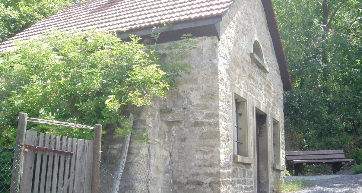 Kleines Steinhaus mit Ziegeldach, umgeben von Bäumen. Ein Holzzaun und eine Bank sind sichtbar. Es wirkt ländlich und ruhig., © Land der 1000 Hügel - Kraichgau-Stromberg Kleines Steinhaus mit Ziegeldach, umgeben von Bäumen. Ein Holzzaun und eine Bank sind sichtbar. Es wirkt ländlich und ruhig., © Land der 1000 Hügel - Kraichgau-Stromberg