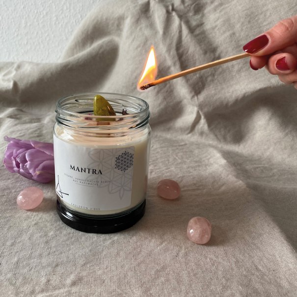 Eine Hand mit rotem Nagellack zündet eine Kerze im Glas an. Umgeben von rosa Steinen und einer Blume auf beigem Stoff., © Mercedes-Benz AG Eine Hand mit rotem Nagellack zündet eine Kerze im Glas an. Umgeben von rosa Steinen und einer Blume auf beigem Stoff., © Mercedes-Benz AG