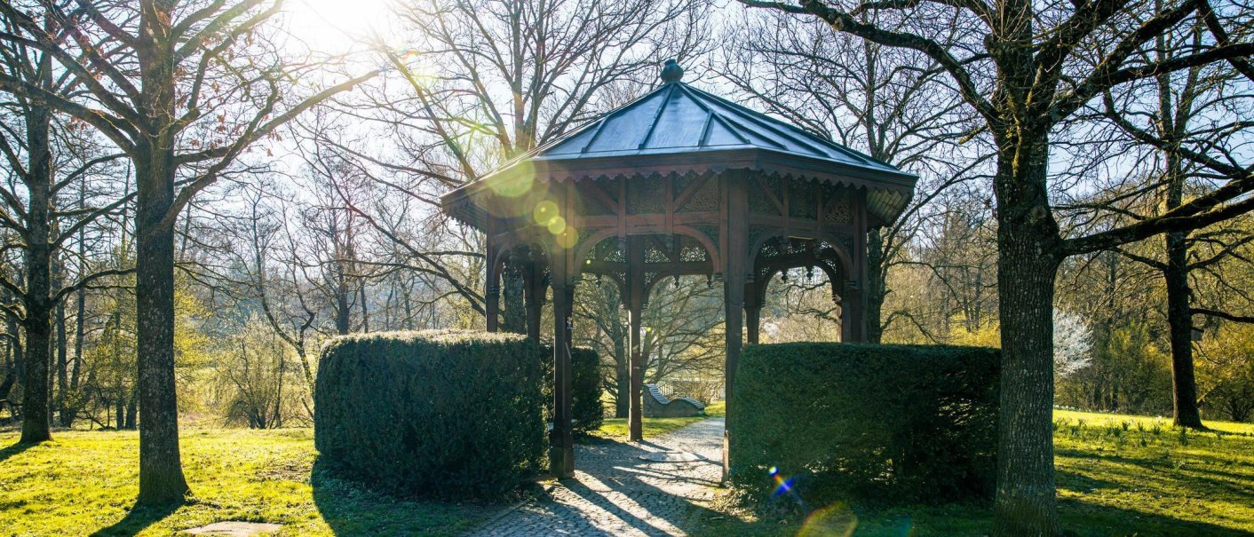Ein Pavillon im Sommerhofenpark, umgeben von B&auml;umen und Str&auml;uchern. Die Sonne scheint durch die &Auml;ste und erzeugt Lichtreflexe., &copy; Stuttgart-Marketing GmbH, Sarah Schmid