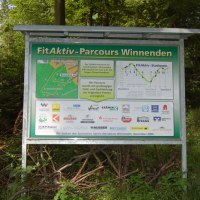 Schild des FitAktiv-Parcours Winnenden im Wald. Es zeigt eine Karte des Parcours und Logos von Sponsoren. Der Weg führt durch bewaldetes Gebiet., © Winnenden - Stuttgart-Marketing GmbH
