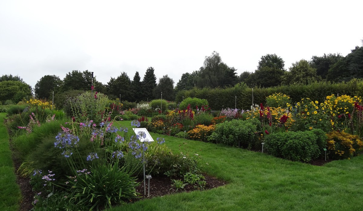 Ein gepflegter Garten mit bunten Blumenbeeten, grünem Rasen und Bäumen im Hintergrund unter bewölktem Himmel., © Nürtingen - Stuttgart-Marketing GmbH