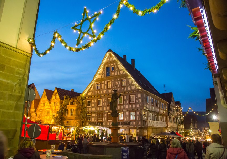 Weihnachtsmarkt in einer Altstadt mit beleuchteten Fachwerkhäusern und festlicher Dekoration. Menschen schlendern durch die Stände bei Abenddämmerung., © Stadt Besigheim Weihnachtsmarkt in einer Altstadt mit beleuchteten Fachwerkhäusern und festlicher Dekoration. Menschen schlendern durch die Stände bei Abenddämmerung., © Stadt Besigheim
