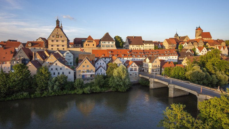 Die Altstadt von Besigheim mit ihren historischen Gebäuden und roten Dächern, umgeben von einem Fluss und einer Brücke im Vordergrund., © Unbekannt Die Altstadt von Besigheim mit ihren historischen Gebäuden und roten Dächern, umgeben von einem Fluss und einer Brücke im Vordergrund., © Unbekannt