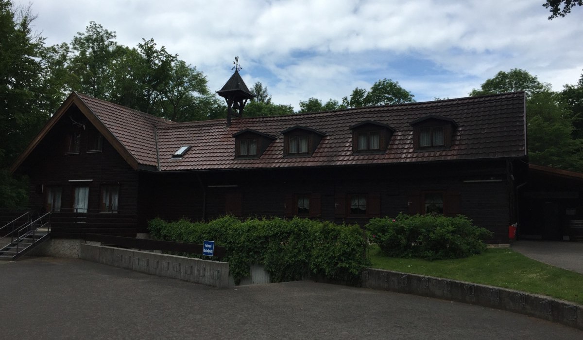 Rustikale Holzhütte mit Satteldach und Dachgauben, umgeben von Bäumen. Der Himmel ist bewölkt., © www.pro-cycl.de