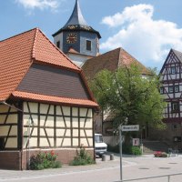 Fachwerkhäuser in Gündelbachs Ortsmitte, mit einem Kirchturm im Hintergrund. Ein Straßenschild zeigt 'Winzerstraße'. Sonniger Tag mit blauem Himmel., © Land der 1000 Hügel - Kraichgau-Stromberg Fachwerkhäuser in Gündelbachs Ortsmitte, mit einem Kirchturm im Hintergrund. Ein Straßenschild zeigt 'Winzerstraße'. Sonniger Tag mit blauem Himmel., © Land der 1000 Hügel - Kraichgau-Stromberg