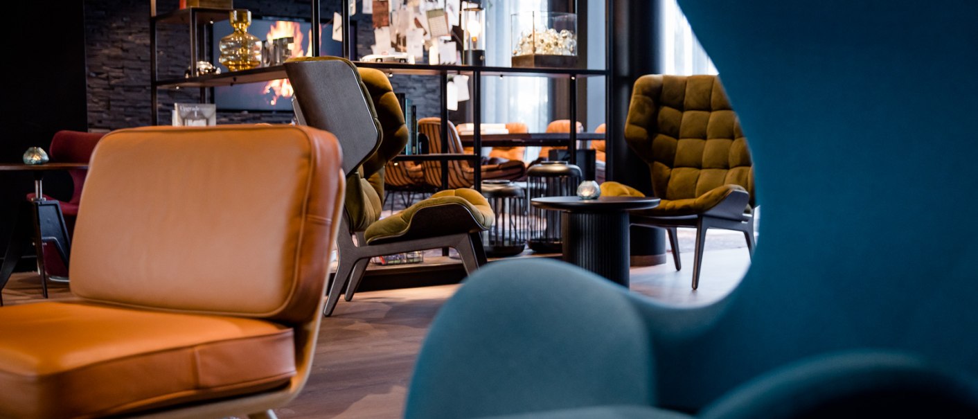 Moderne Lounge mit stilvollen Sesseln in Blau und Braun, Regalen mit Dekorationen und gemütlicher Atmosphäre., © TOMAS