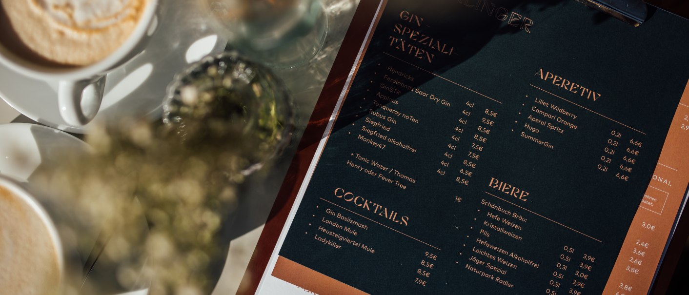 Speisekarte mit Getränken wie Gin, Cocktails und Bier, daneben eine Tasse Kaffee. Elegantes Design mit dunklem Hintergrund und goldener Schrift., © L. Prestle/ Documenting Love Speisekarte mit Getränken wie Gin, Cocktails und Bier, daneben eine Tasse Kaffee. Elegantes Design mit dunklem Hintergrund und goldener Schrift., © L. Prestle/ Documenting Love