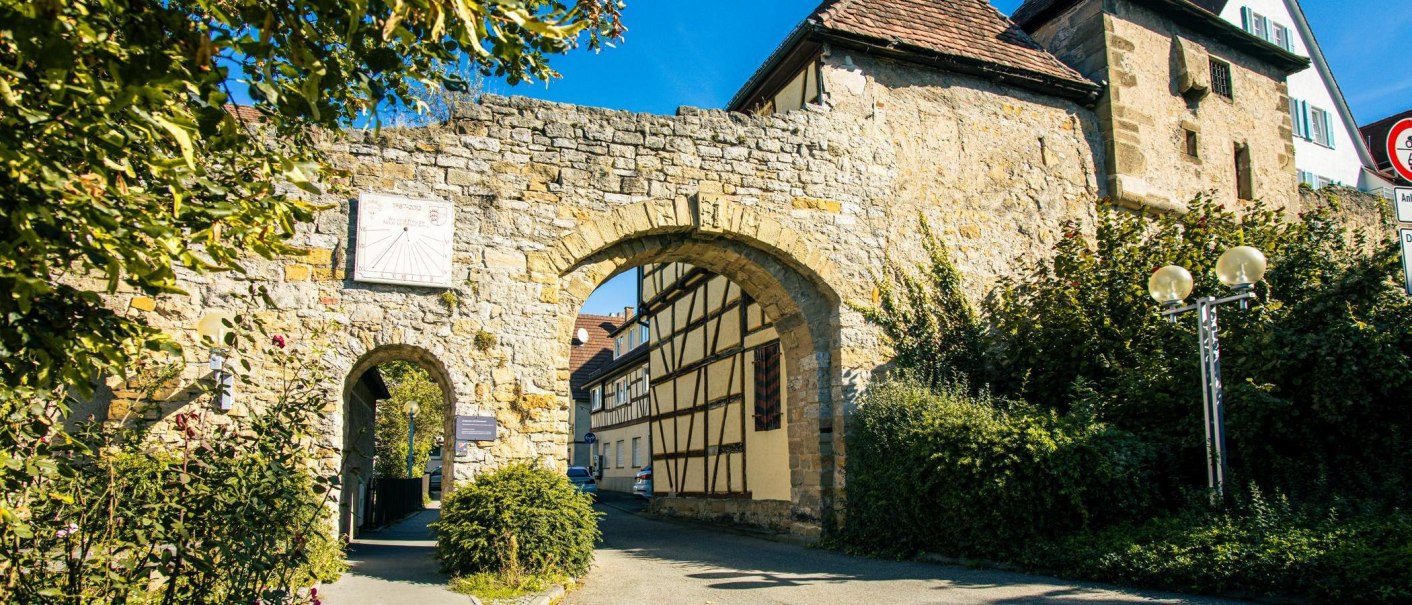 Ein altes Stadttor in Marbach am Neckar, flankiert von Fachwerkhäusern und umgeben von grüner Vegetation unter blauem Himmel., © Stuttgart-Marketing GmbH, Sarah Schmid