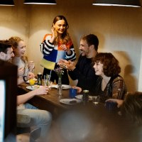 Eine Gruppe von Menschen sitzt in einem Café um einen Tisch und lacht. Eine Frau steht und spricht mit den anderen. Die Atmosphäre ist gemütlich., © Stuttgart Marketing GmbH, Alwin Maigler Eine Gruppe von Menschen sitzt in einem Café um einen Tisch und lacht. Eine Frau steht und spricht mit den anderen. Die Atmosphäre ist gemütlich., © Stuttgart Marketing GmbH, Alwin Maigler