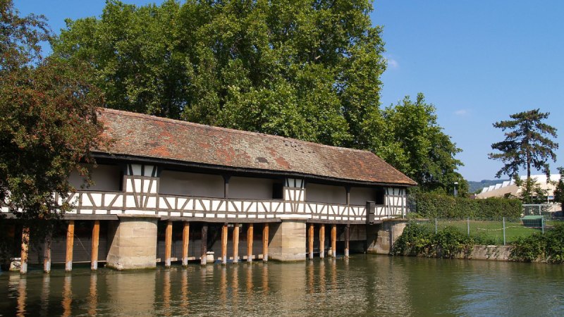 Fachwerkbrücke über den Neckar in Esslingen, umgeben von Bäumen und Wasser. Der Himmel ist klar und blau., © Thomas Krebs