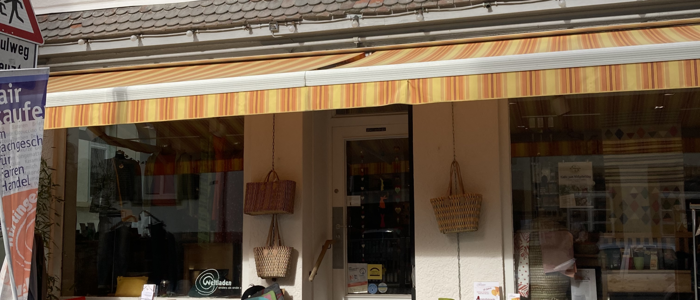 Ein kleiner Laden mit bunten Tischen und Stühlen vor der Tür. Eine Markise spendet Schatten. Im Schaufenster sind Körbe und Dekorationen zu sehen., © L. Besmer