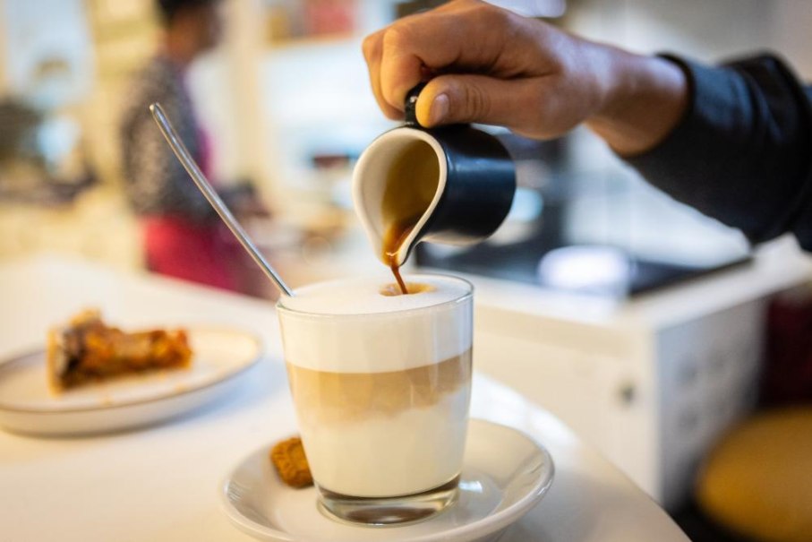 Eine Hand gie&szlig;t Espresso in ein Glas mit Milchschaum. Im Hintergrund steht ein Teller mit Kuchen auf einem Tisch., &copy; Ludwigsburg Museum